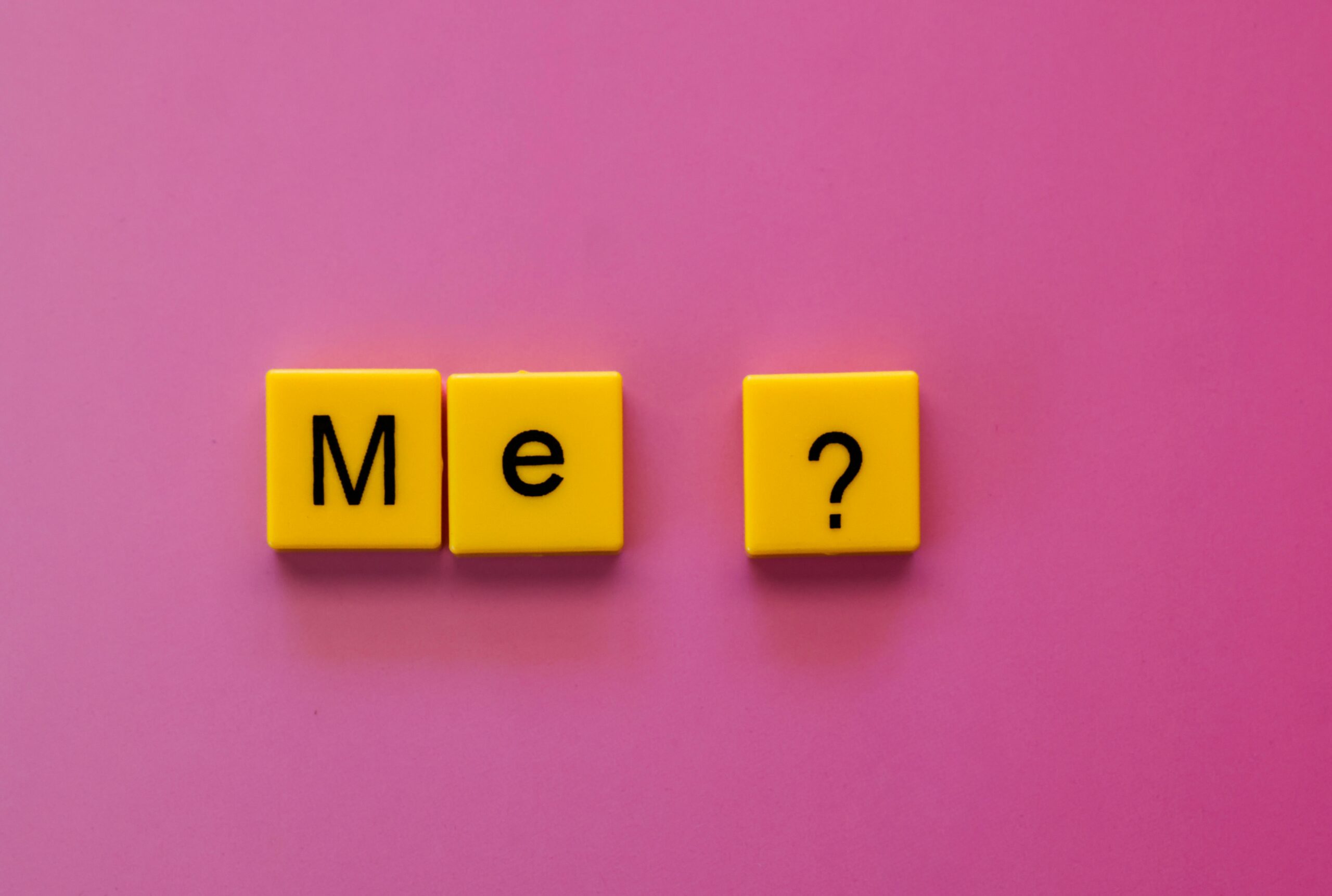 Yellow letter tiles spelling 'Me?' on a pink background, illustrating the challenge of showing up authentically.